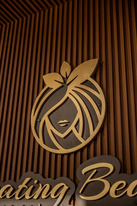 Gold and gray stylized female face logo with a bow on a wooden slat background