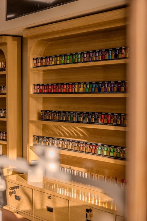 Wooden shelving unit displaying organized rows of colorful nail polish bottles with wooden storage cabinet below