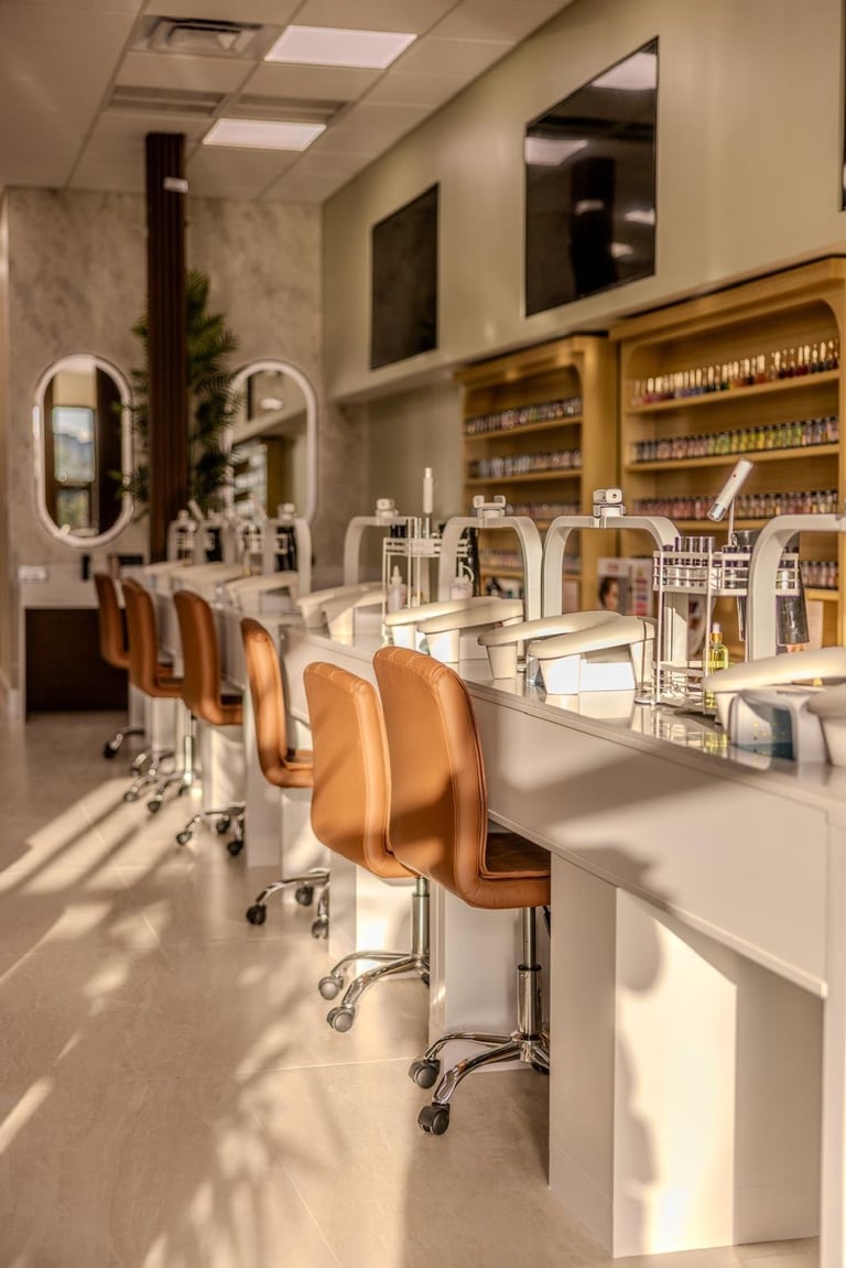 Modern beauty salon interior with white workstations, tan leather chairs, gold shelving, and oval mirrors along the wall