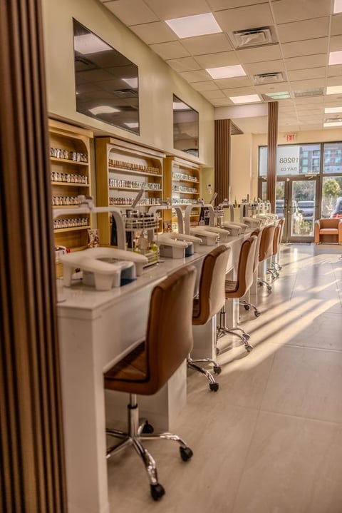 Modern salon interior with row of styling stations, tan and wood chairs, shelving with products, and glass windows